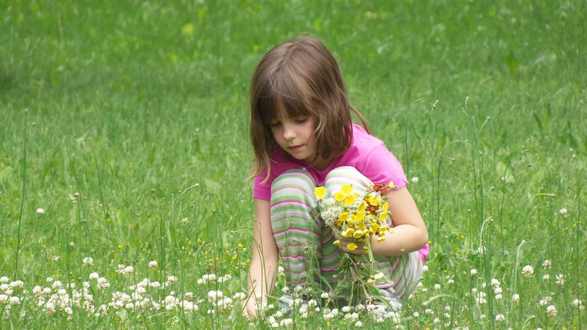 Child kneeling by a bird feeder writing in a nature journal after spotting a backyard bird